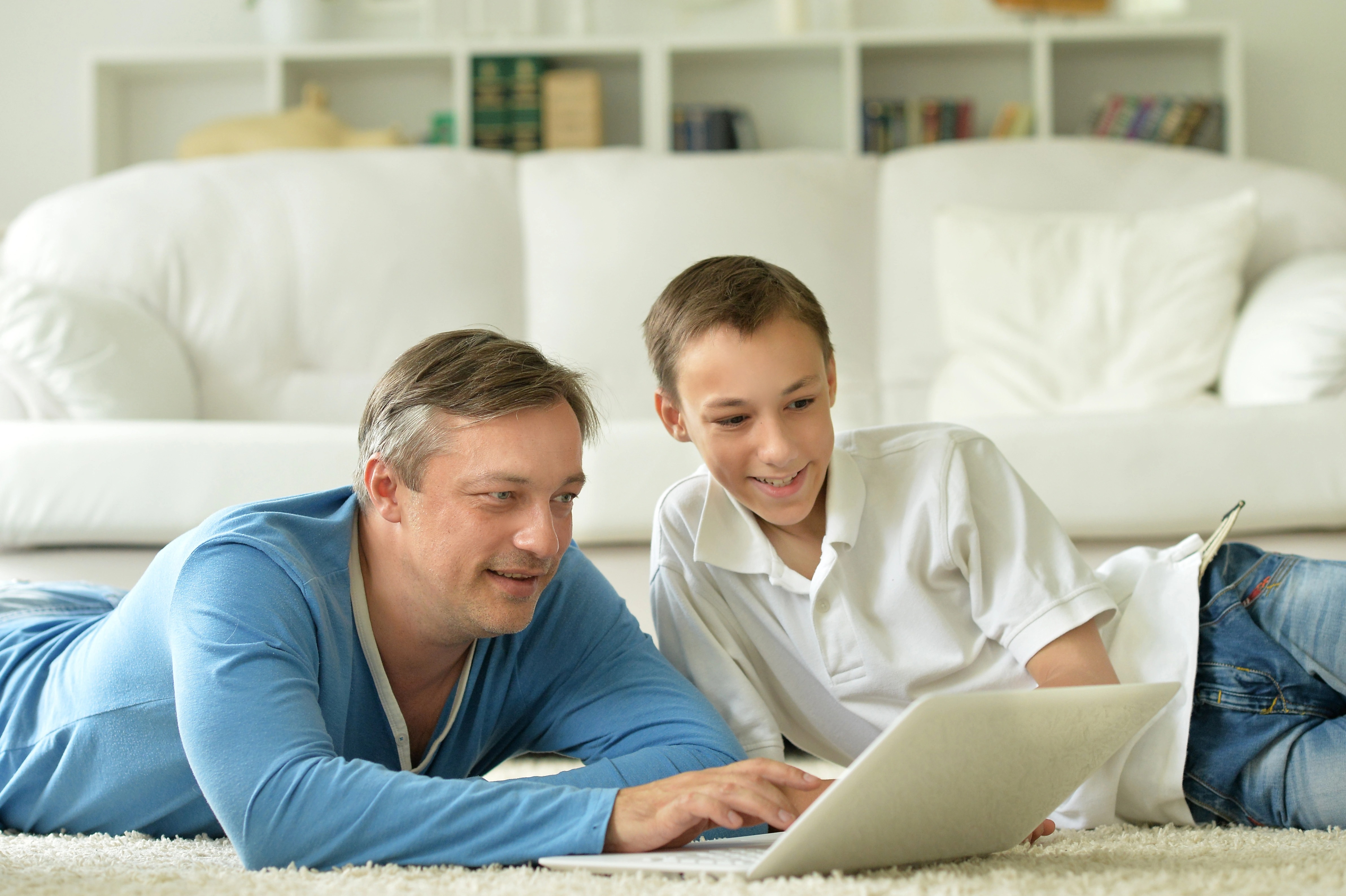 Man typing on laptop on the floor with a boy smiling