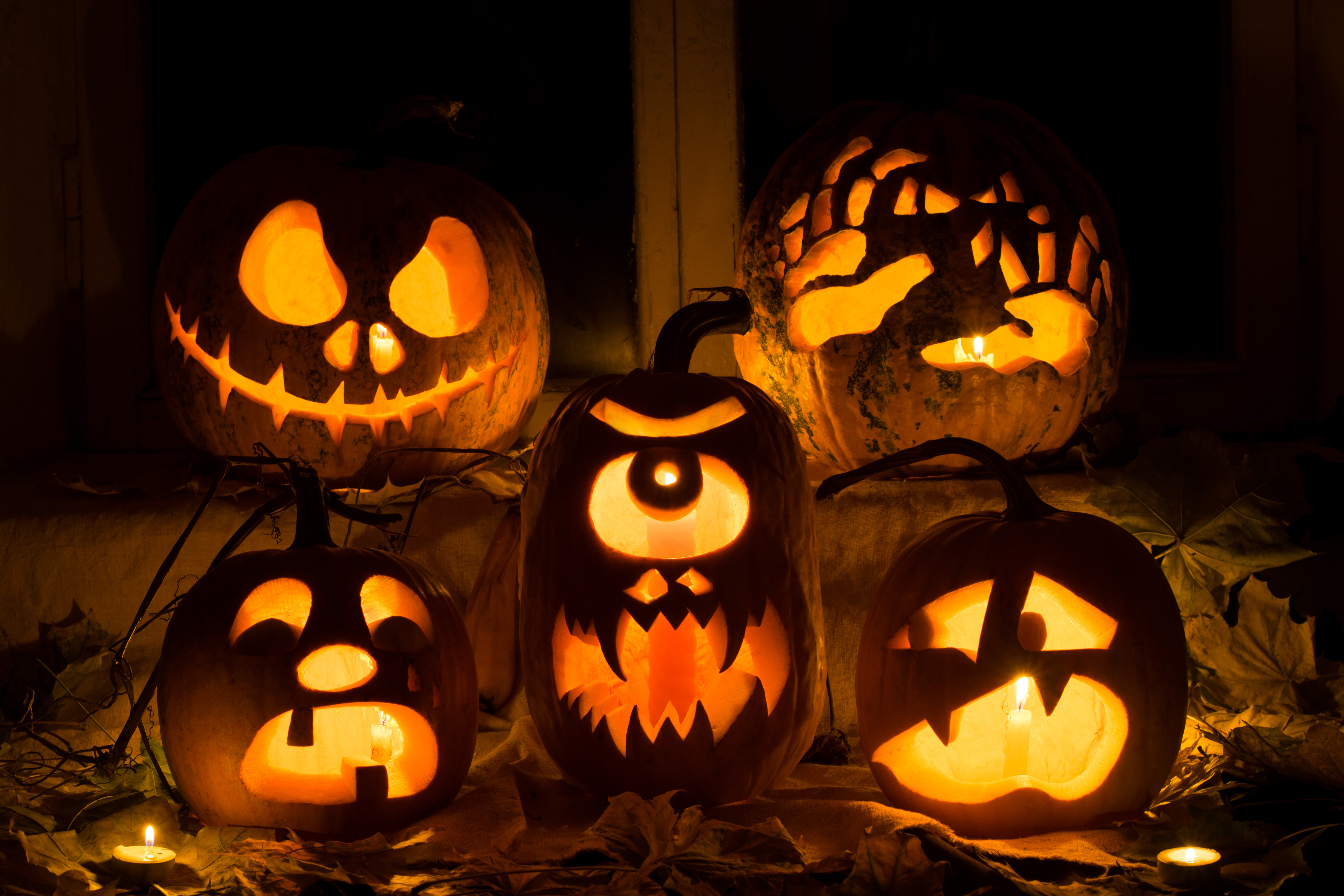 Photo composition from five pumpkins for Halloween. Jack, hands, crying, a Cyclops and frightened pumpkins against autumn leaves and candles