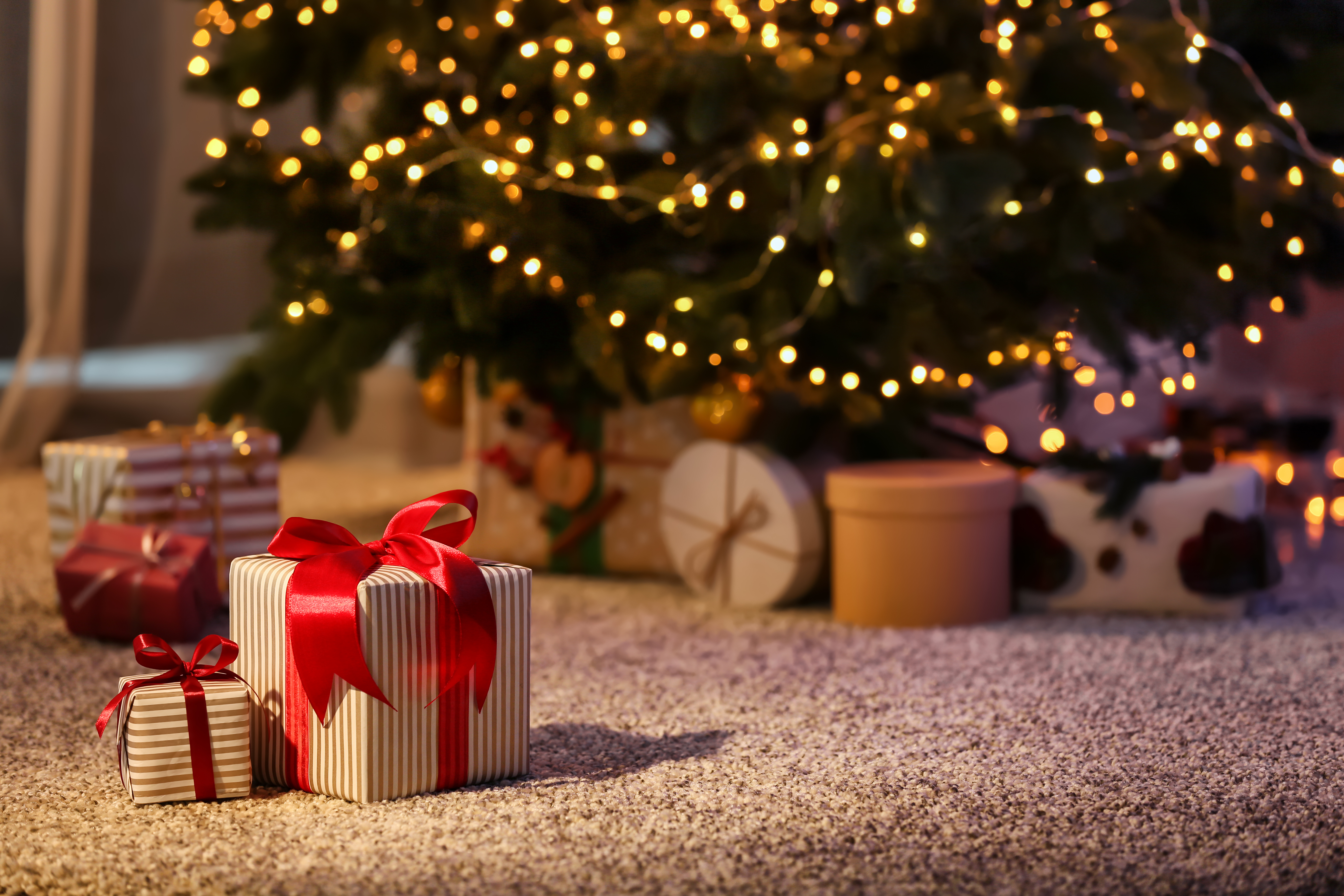 Beautiful Christmas gift boxes on floor near fir tree in room