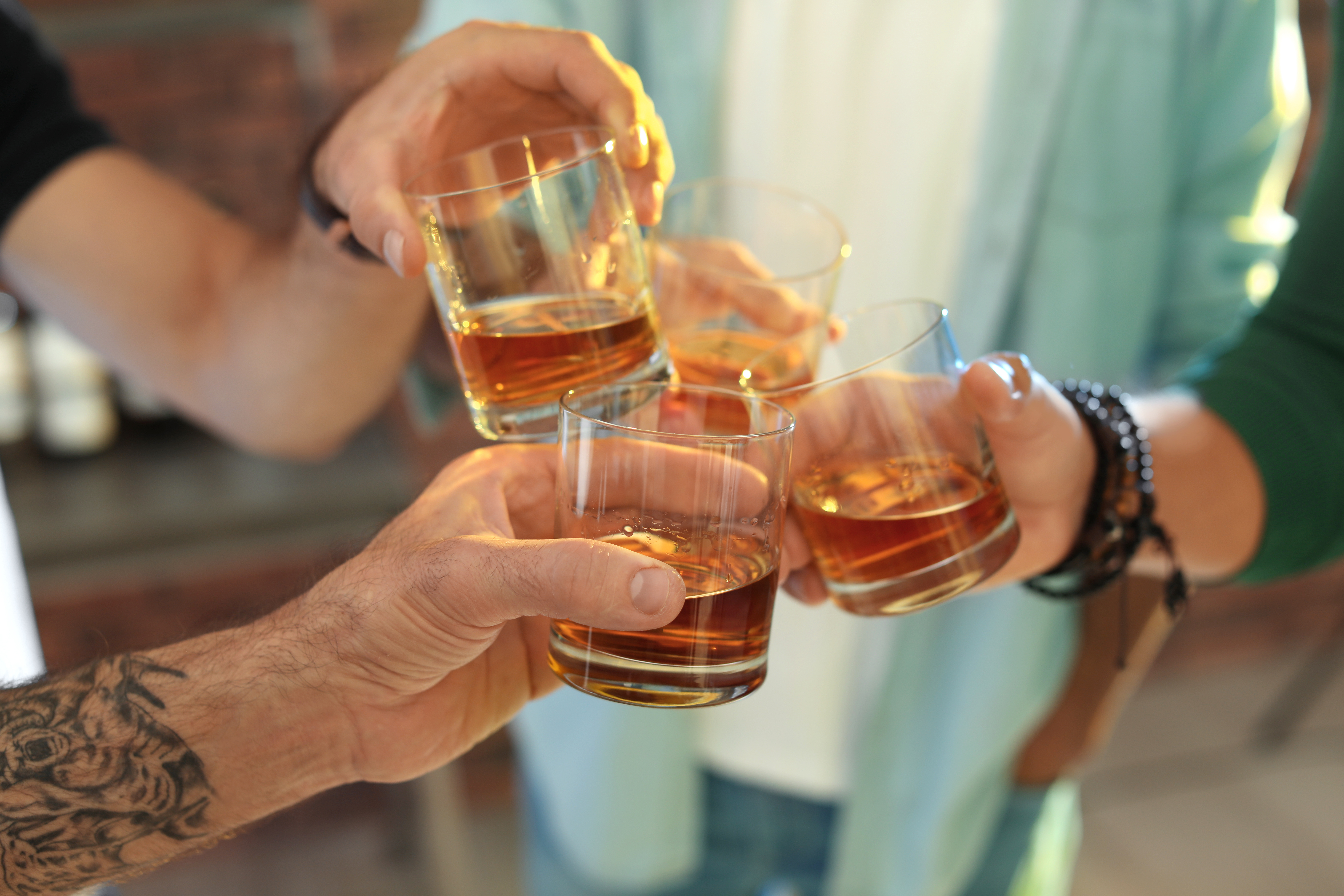 Friends toasting with glasses of whiskey indoors, closeup